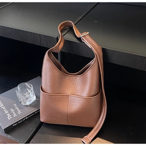 Detail showing the deep brown lychee texture and two front pockets of the bucket bag