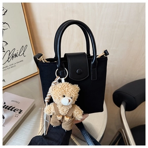 Detail of black canvas bucket bag with leather handle and cute plush bear charm
