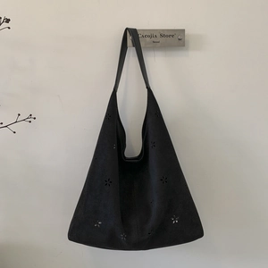 Close-up of black suede tote bag with laser-cut floral patterns and premium leather strap