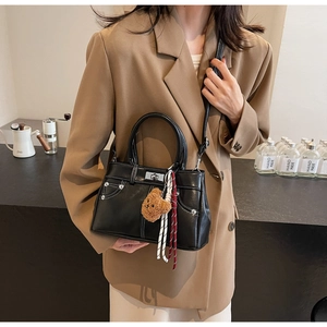 Detail of black PU leather handbag with white stitching and a cute teddy bear charm