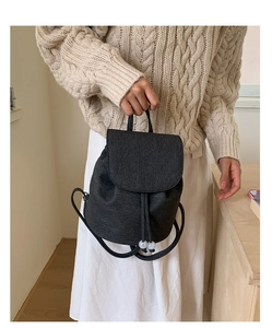 Detail of black canvas backpack featuring drawstring closure and white bead decorations