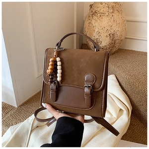 Detail of vintage brown leather backpack with buckle straps and wooden bead charm accessory