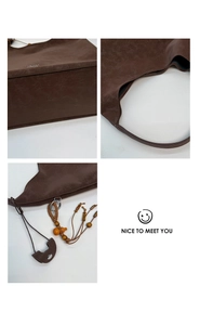 Detail of dark brown leather tote featuring brand logo and woven beaded tassel charm