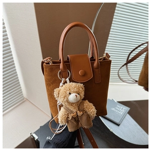 Detail of suede crossbody bucket bag featuring a plush bear charm and leather strap