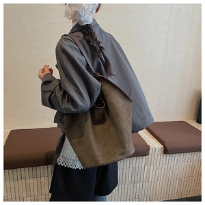 Olive green frosted tote bag worn by a model against a minimalist wooden wall background