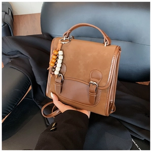 Detail view of a vintage brown leather backpack featuring bead charms and metal buckles