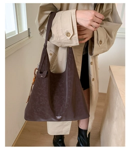 Detail of a large brown canvas tote bag featuring wooden bead charm and logo