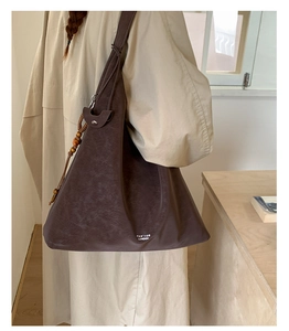 Detail view of a dark brown retro leather tote bag with wooden bead charm and logo