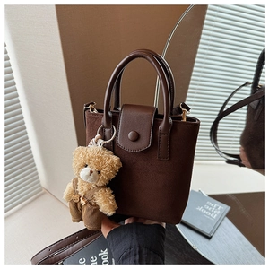 Detail of dark brown faux suede tote bag with leather handles and a cute teddy bear charm