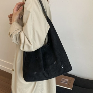 Detail of laser-cut floral pattern on black suede tote bag with minimalist shoulder strap