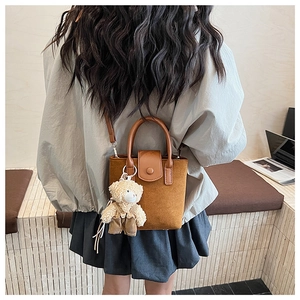 Detail of brown frosted bucket bag featuring a cute teddy bear charm and magnetic flap