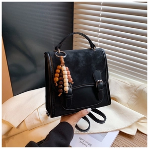 Close-up of black retro backpack with matte leather texture and colorful wooden bead tassel