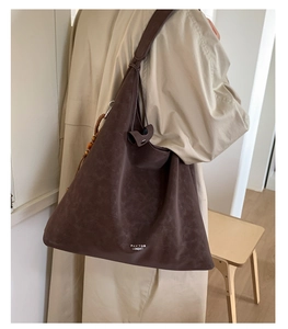 Detail view of a large brown suede tote bag with knot strap and wooden bead accessory