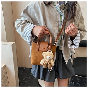 Detail of brown faux suede bucket bag featuring a cute plush teddy bear charm accessory