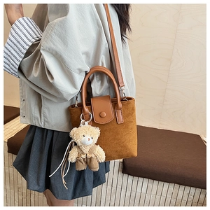 Detail of brown suede bucket bag featuring a cute plush bear pendant and leather strap