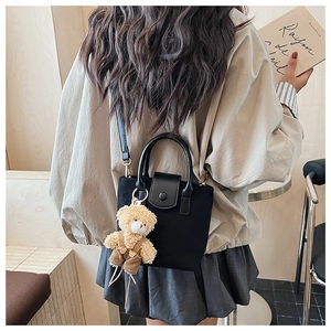 Detail of matte black crossbody bag with a cute brown plush bear charm and leather handle