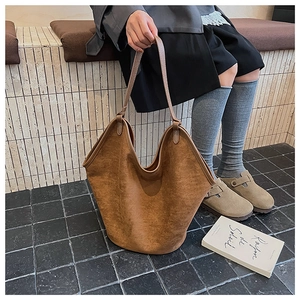 Detail of a large caramel suede bucket bag held by a model on stairs for a chic commute