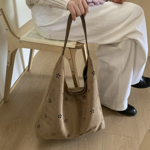 Detail of laser-cut floral patterns on camel suede tote bag with dark brown leather strap