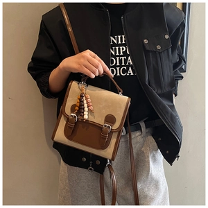 Close-up of a vintage dual-tone shoulder bag with metal buckles and a wooden bead charm