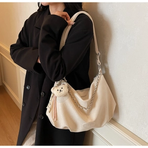 Détail d'un sac hobo beige avec chaîne argentée, breloque ours en peluche et large bandoulière