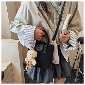 Detail of black canvas bucket bag with plush bear charm and leather shoulder strap