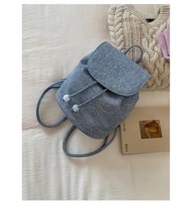 Detail of grey-blue textured backpack with drawstring closure and white pom-pom charms