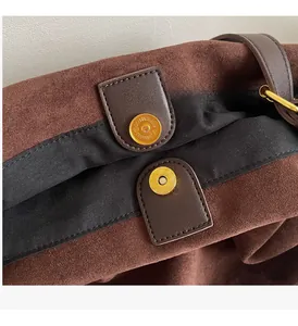 Detailed macro of the gold magnetic closure on a brown suede bucket bag with black lining