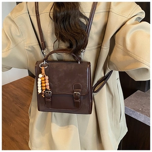 Detail of vintage brown leather backpack featuring dual buckles and colorful beaded charm