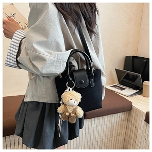 Close-up of black crossbody bucket bag featuring a cute teddy bear plush charm detail