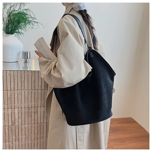 Detail view of large matte black tote bag on a trench coat model in a lifestyle setting
