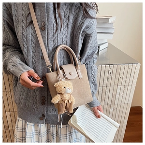 Close-up of a khaki frosted suede bucket bag with a cute bear charm on a grey cardigan