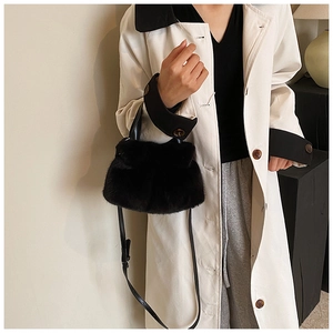 Gros plan du sac seau en peluche noire porté avec un trench-coat d'automne minimaliste