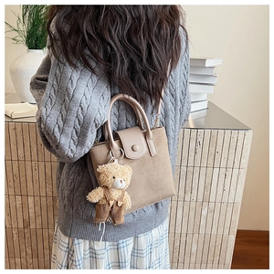 Detail view of brown matte bucket bag with a cute teddy bear plush charm and strap