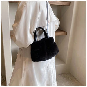 Détail d'un sac seau en fausse fourrure noire porté avec un trench-coat crème