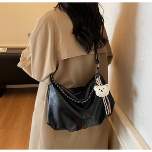 Détail d'un grand sac hobo en cuir noir avec chaîne argentée et breloque ourson
