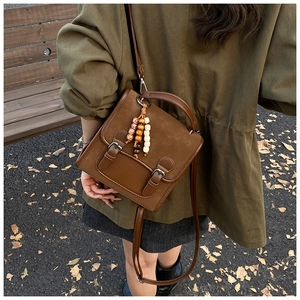 Detail of vintage caramel brown backpack with buckle straps and bead charm in outdoor setting