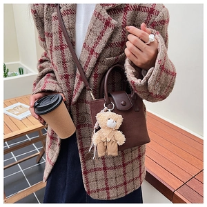 Detail of dark brown suede crossbody bag with a cute teddy bear plush charm