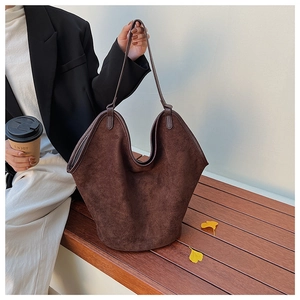 Detail of dark brown suede tote bag with U-shaped opening held in an autumn setting