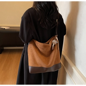 Detail of tan suede bucket bag with dark brown leather base and plush ball charm