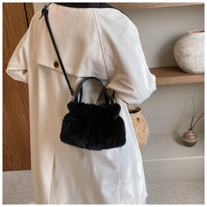 Détail d'un sac seau noir en peluche avec poignées en cuir sur un manteau blanc