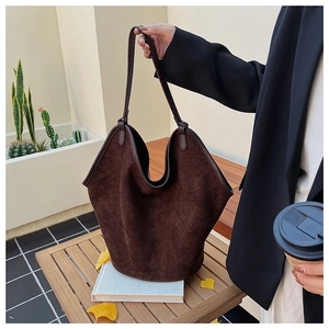 Close-up of a large dark brown matte suede tote bag held by a model in a cozy balcony setting
