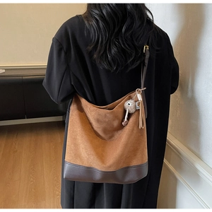 Detail of hobo bag in brown suede and leather patchwork with plush ball pendant