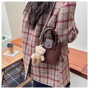 Close-up of brown suede crossbody bucket bag with cute bear charm and vintage texture