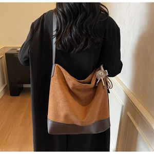 Rear view of model wearing a brown suede tote bag with leather straps and plush charm