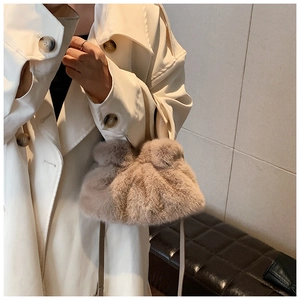 Détail macro d'un sac nuage en fausse fourrure beige porté avec un manteau chic beige