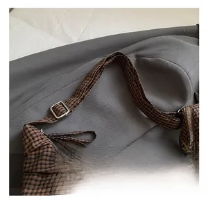 Detail of adjustable shoulder strap with silver buckle on brown plaid underarm bag