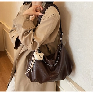 Détail du sac hobo en cuir marron foncé avec chaîne argentée et breloque ours en peluche