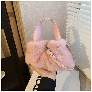 Détail d'un sac seau rose en peluche avec bandoulière en cuir sous une lumière douce