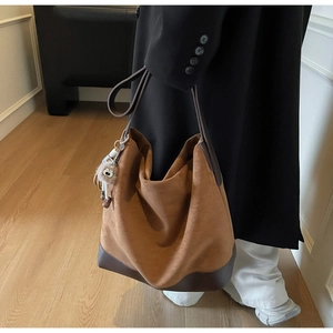 Detailed side view of large brown suede tote bag with leather base and bear charm