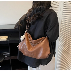 Détails d'un sac cabas marron avec chaîne en métal et breloque ours en peluche porté